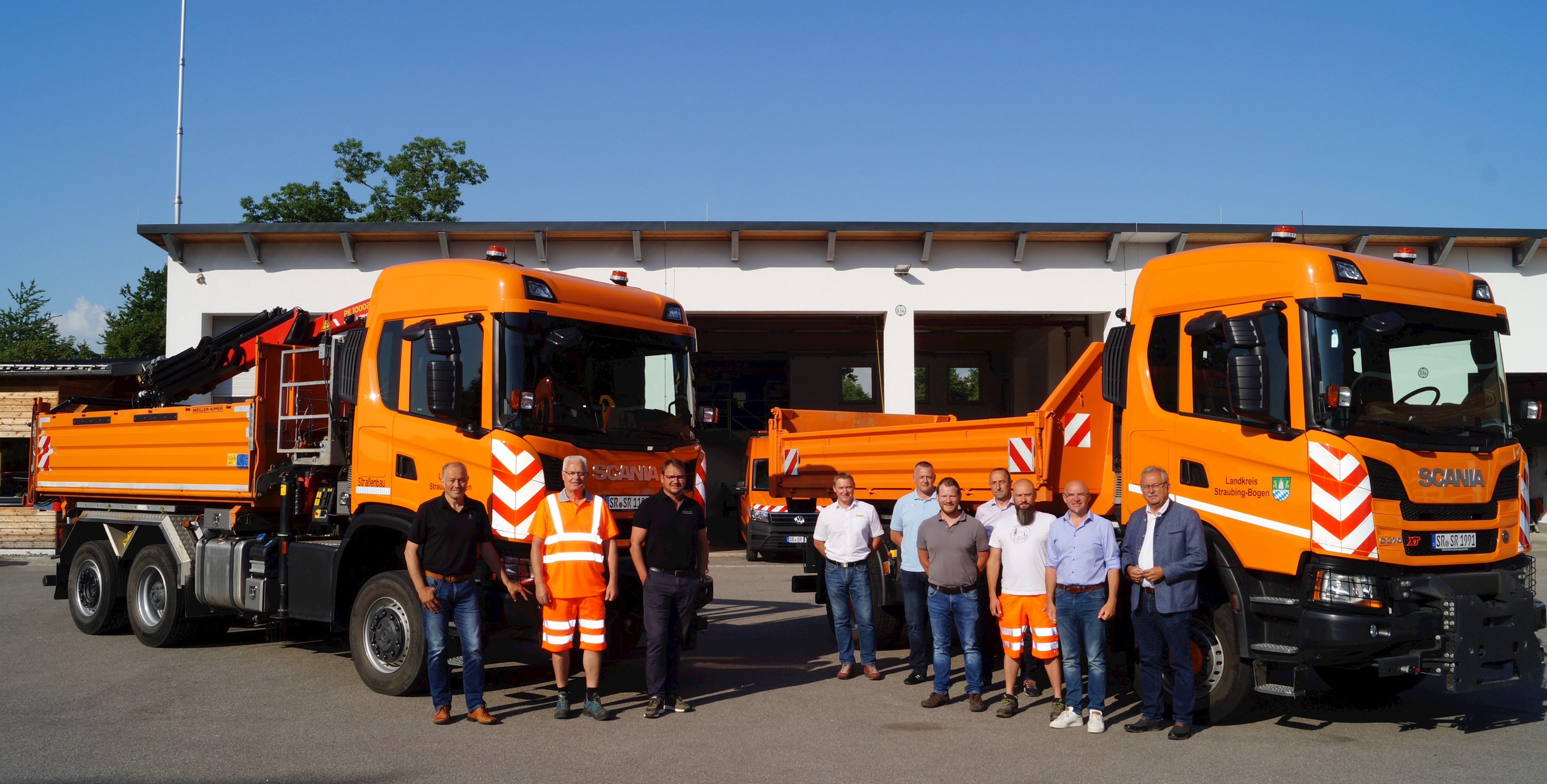 Landrat Laumer steht gemeinsam mit Vertretern der Firmen, des Tiefbauamtes und den Straßenmeistern und Fahrern im Bauhof in Bogen vor den beiden neuen Fahrzeugen.